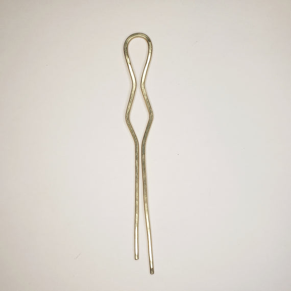hammered brass hairpin on neutral background. hairpin features two prongs, a cylindrical loop at the top, and a triangular symmetrical shape in the middle