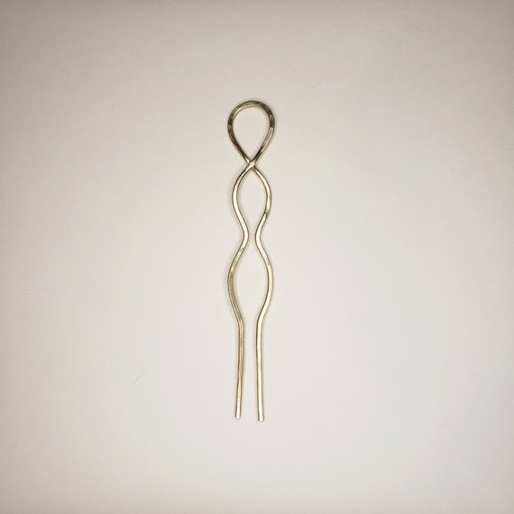 hammered brass hairpin on white background. the hairpin has two prongs, a crossover loop at the top and two symmetrical round waves in the metal