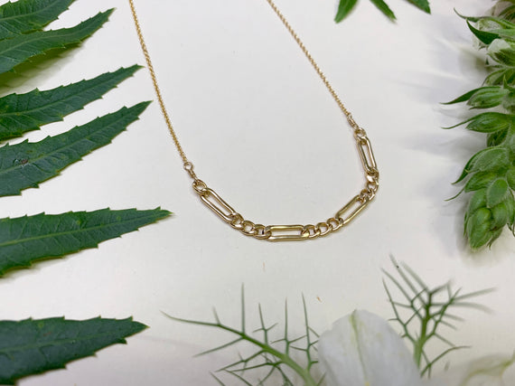 small section of thick gold Figaro chain wrapped between two pieces of delicate gold chain