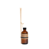 amber glass bottle with brown paper label with a bundle of wooden reed sticks rubber banded to bottle