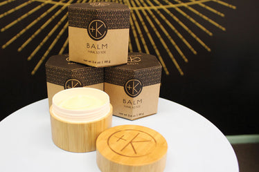 bamboo jar holding cream with logo engraved into lid. behind is a brown cardboard box that holds the jar and has the branding and product name. 