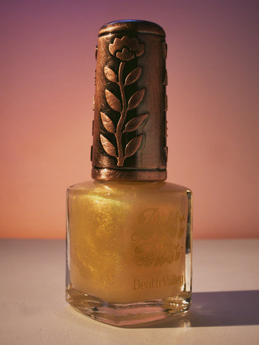 nail polish bottle on sunset toned background with decorative bronze top showing engraved flower shape 
