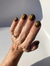 nail polish swatch on fair skinned hand colour is green and gold and reflective￼