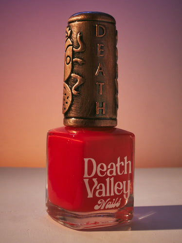 nail polish bottle in Sunset toned background with decorative bronze cap featuring the word is death Valley and a beetle sitting on a ball￼