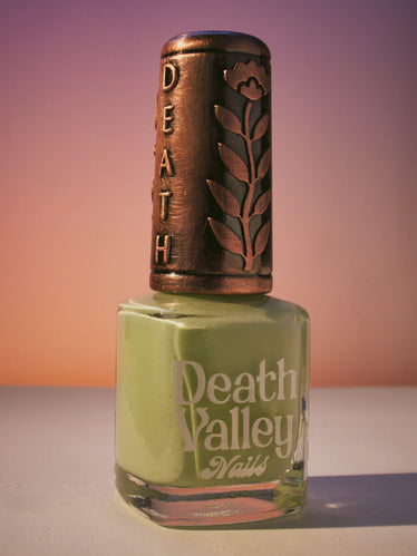 Nail polish bottle in Sunset toned background featuring a decorative bronze cap with the words death Valley and an engraved flower