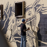 Image of Jess painting a mural on a large brick wall￼