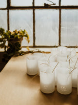 Empty frosted glass jars with wicks on a wood counter waiting to be filled with wax 