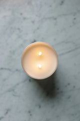 Birdseye view of a candle with two wicks that are lit on a marble countertop