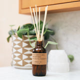 reed diffuser sitting on counter next to plant pot and crystal 