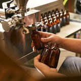 Man’s hands holding amber glass bottles filling them with scented oil from a stainless steel machine