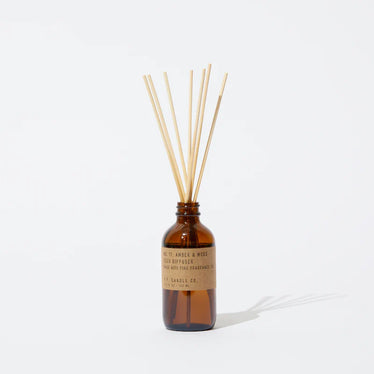 amber glass jar with brown paper label holding wooden sticks to dispense scent. 