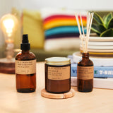 A Golden Coast room spray sitting next to a Golden Coast candle and the Golden Coast read diffusers on a coffee table next to a plant and a lamp￼