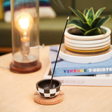 A stick incense burning in a little dish on a coffee table next to a lamp and plant￼