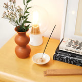 stick incense burning in dish on table with flowers lamp and books