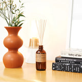 reed diffuser bottle sitting on table next to vase and books
