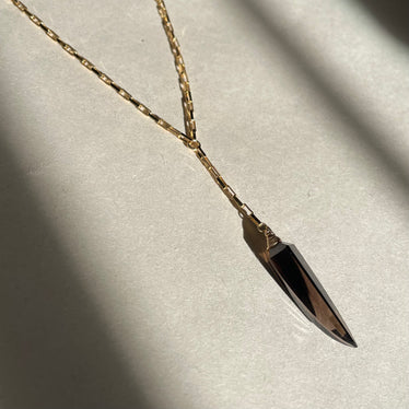 Necklace with a black dagger pendant on a light gray background