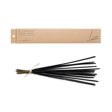 A bundle of black incense tied together with twine next to a brown cardboard box that they come in￼