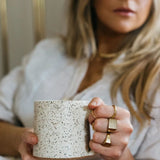 Woman holding mug wearing various rings including Roam signet ring