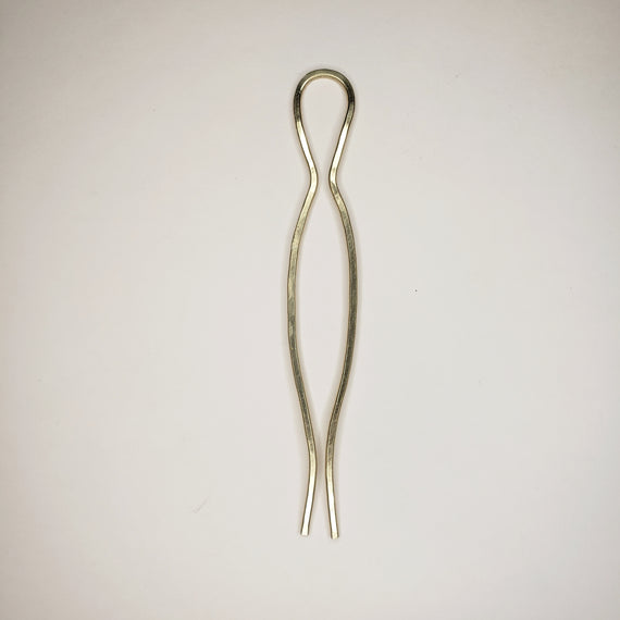And hammered brass hairpin on neutral background the hairpin features two prongs symmetrical with one big curve in the middle