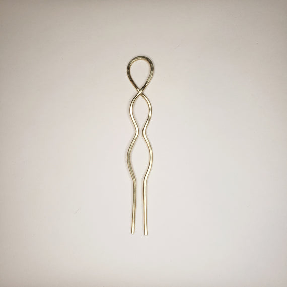 hammered brass hairpin on white background. the hairpin has two prongs, a crossover loop at the top and two symmetrical round waves in the metal 