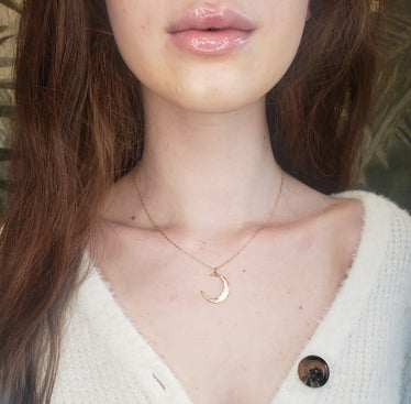 Woman wearing gold crescent moon necklace necklace hits just below the collarbone and reflects light beautifully