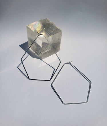 Two large Pentagon hoops lay on a neutral background one line against a cubic crystal