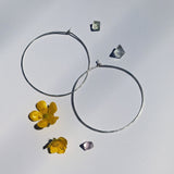 Two large circle hooks on a white background with crystals and flowers the hoops are a thin silver that his hand hammered