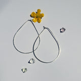 Large teardrop hoops laying on a neutral background with crystals and flour the teardrop hoops are rounded at the bottom pointed at the top and hand hammered