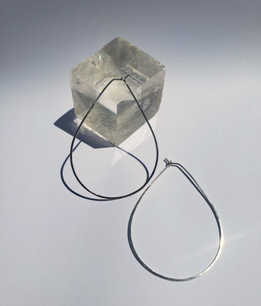 large teardrop hoops laying on a neutral background one laying against a cubic crystal￼
