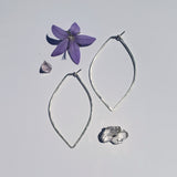 two large petal hoops laying a neutral background with a flower and crystals the hoops are a pointed teardrop shape and hand hammered￼