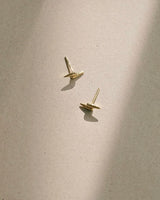 Two gold toned studs on a grey background. The studs are two sharp cylinders offset to look similar to a lightening bolt. 