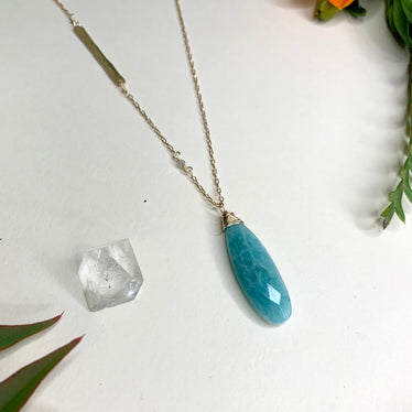 Detail shot of amazonite stone pendant hanging off necklace. The stone is a light turquoise blue with subtle white markings in stone. 