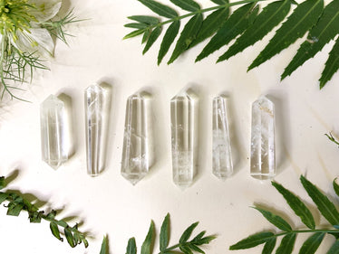 six double sided quartz points, one end slightly larger than the other,  laid out on a cream background with leaves￼