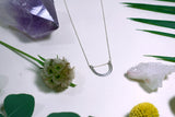 flat lay of sterling silver double arc necklace on white background next to flowers and crystals￼