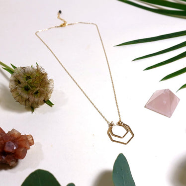 double hexagon necklace laying flat on cream background with leaves and crystals￼
