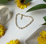 Figaro chain bracelet clasped laying flat on a white background with flowers surrounding￼