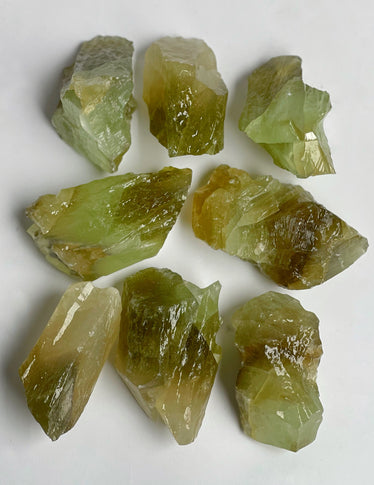 Nine medium green calcite crystals laying on a neutral background showing the green tones going from a mossy green to a lime green reflecting light