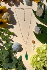 Diamond drop necklace laying flat on cream background with Flowers and crystals. the necklace features pyrite beads cut into the chain and a green onyx diamond shape￼d stone