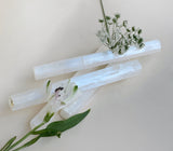 Close up photo of medium-sized selenite sticks showing bright white flashes in the light with flowers