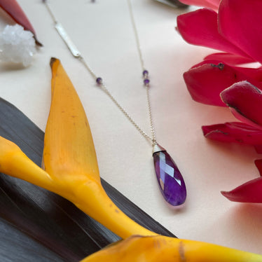 A close up photo of the amethyst teardrop pendant. Light reflecting off the various lapidary cuts in the stone 