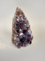 Side view photo of medium amethyst cluster on a neutral background. wide at the bottom pointed at the top with large crystals formations