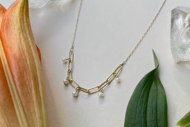 five miniature seed pearls that hang off a section of paperclip chain that hangs in the middle of a fine delicate gold chain￼