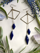two earrings featuring horizontal diamond shapes with two diamond shaped stones of lapis hanging off of gold chains from the top of the earring￼