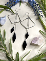 two earrings featuring horizontal diamond shapes with two diamond shaped stones of black onyx hanging off of silver chains from the top of the earring