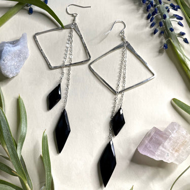two earrings featuring horizontal diamond shapes with two diamond shaped stones of black onyx hanging off of silver chains from the top of the earring
