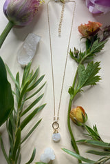 necklace laying on a white background the necklace features a rounded rainbow moonstone hanging off of a hammered gold circle connected to the chain with two small moonstone beads￼