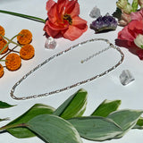 flat lay image of full sterling silver Figaro chain on white background with flowers￼