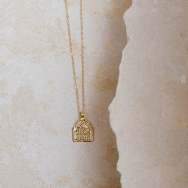 Gold pendant necklace on stone background necklaces on a dainty gold chain featuring a pendant resembling a Roman building￼