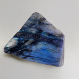 Close upshot of medium labradorite slab on neutral background one side is polished showing beautiful blue flashes with lines of white flash
