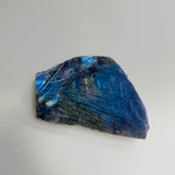 Large chunk of labradorite polished on one side laying on a neutral background